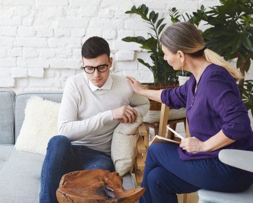 candid-shot-casually-dressed-professional-woman-psychotherapist-her-fifties-touching-her-young-male-patient-by-shoulder-while-having-counseling-session-expressing-sympathy-support candid-shot-casually-dressed-professional-woman-psychotherapist-her-fifties-touching-her-young-male-patient-by-shoulder-while-having-counseling-session-expressing-sympathy-support